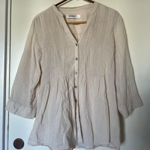 Beige skjorta/blus - Luftig beige skjorta/blus från Mingel ned sömdetaljer framtill. V-ringning, knappar hela vägen och trekvartsärmar med knappdetalj. Köpt second hand. Passar s/m.