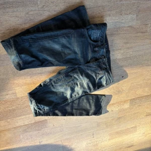 Mörkblå jeans från G-Star RAW 27 34 - Snygga mörkblå jeans från G-Star RAW med coola slitningar och klassisk femficksdesign. Jeansen har raka ben och detaljerad söm på baksidan. Perfekt för dig som gillar streetwear och vill ha en stilren look.