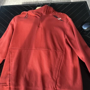 Röd hoodie från Puma med half zip - Snygg röd hoodie från Puma med half zip och huva med snörning. Tröjan har lång ärm, praktisk ficka framtill och en cool logga på bröstet. Materialet är mjukt och känns som bomull och polyester. Perfekt för chill dagar eller när du vill ha en sportig look.