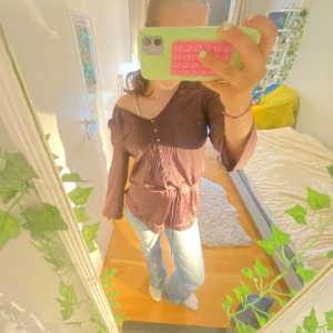 Brun blus med broderi och knyt i midjan - Säljer en brun blus från Stockh lm med v-ringning, broderade detaljer vid halsen och knappar framtill. Blusen har långa ärmar, knytband i midjan och är gjord i ett glansigt, mjukt material som känns lyxigt. Perfekt för dig som gillar romantiska detaljer och relaxed fit.