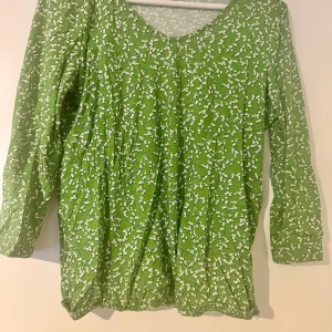 Grön blommig blus från Tom Tailor XS - Säljer en grön blus från Tom Tailor i storlek XS med vitt blommönster. Blusen har lång ärm, v-ringad hals och är tillverkad i en mjuk mix av bomull och modal. Perfekt för dig som gillar färg och mönster i garderoben!