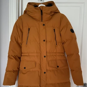 Brun pufferjacka från Everest, stl 36 - Snygg brun pufferjacka från Everest med huva och svarta detaljer. Jackan har dragkedja och knappar framtill, två bröstfickor med dragkedja och två stora fickor med lock. Perfekt för kalla dagar och riktigt skön passform. Helt i nyskick - knappt använd 🧡