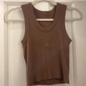 Ribbad brun linnetopp - Säljer en ribbad brun linnetopp med breda axelband och rund halsringning. Toppen är ärmlös och har en enkel, stilren design som passar perfekt till jeans eller kjol. Materialet är mjukt och stretchigt för en bekväm passform.