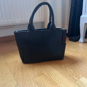 Svart handväska  - Snygg svart handväska med flätad design och två handtag. Väskan har även en avtagbar axelrem och stängs med dragkedja. Perfekt storlek för det viktigaste och ger en stilren look till din outfit. Aldrig andvänder. Hör av er om ni undrar något🩷