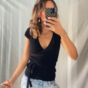 Svart omlottopp med knyt i midjan - Så fin stickad tröja i färgen svart! Den är i storlek S! Tröjan är v ringad och har band vid midjan som man kan knyta!  Vid frågor eller funderingar så är det bara att höra av sig 😊 Bundle = rabatt 💕