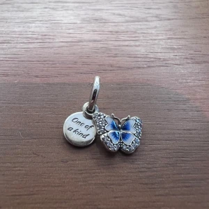Berlock till Pandora armband  - Blå fjäril hängande berlock med ”One of a kind” text i silver till Pandora armband. Så gott som nytt. Använt färre än 10 gånger. (Armband ingår ej i priset)