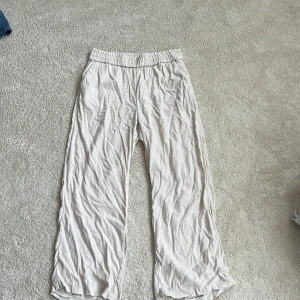 Beiga vida linnebyxor med resår från HM - Luftiga och sköna beiga linnebyxor med resår i midjan och raka, vida ben. Perfekta för varma dagar och enkel stil. Materialet är tunt och svalt, vilket gör dem riktigt bekväma att bära. Litet hål på insidan av benet.