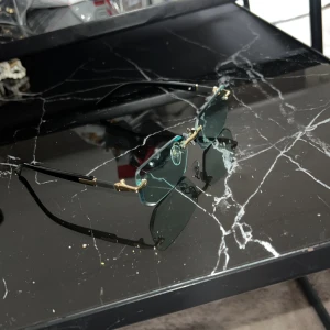 Rektangulära solglasögon med gulddetaljer - Snygga solglasögon med rektangulära, mörkgröna glas och tunna svarta skalmar. Glasögonen har guldfärgade detaljer vid bågarna och näsbryggan för en extra lyxig känsla. Perfekt accessoar för att lyfta din stil.