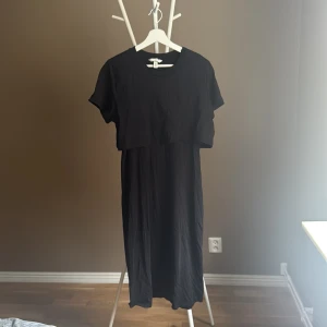 Svart långklänning mamma från H&M - Svart långklänning från H&M i mjuk bomull. Klänningen har korta ärmar och en cool lager-på-lager-effekt upptill som ger en trendig look. Enkel rund halsringning och rak passform, perfekt för dig som gillar minimalistisk stil.🌸