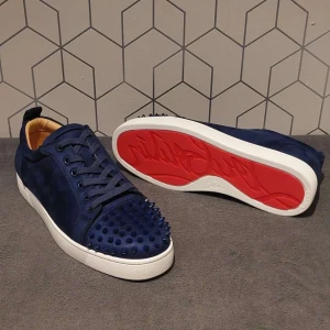 Blå sneakers med nitar från Louboutin - Snygga mörkblå sneakers i mocka från Louboutin med ikoniska röda sulor och coola nitar på tån. Skorna har snörning, vit sula och en riktigt lyxig vibe. Perfekta för dig som vill sticka ut med stil och detaljer.