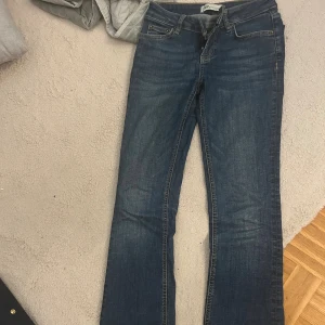 Blå jeans från Zara, bootcut - Snygga blå jeans från Zara med klassisk femficksdesign och bootcut-ben. Jeansen har normalhög midja, dragkedja och knapp framtill samt guldfärgade sömmar. Perfekta för dig som gillar en tidlös denimlook.