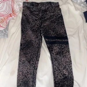Leopardmönstrade leggings från Stronger - Snygga leopardmönstrade leggings från Stronger i svart och grått. De är tillverkade i ett stretchigt material av återvunnen polyester och elastan, med hög midja och bred linning för extra komfort. Perfekta för träning eller chill dagar.