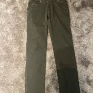 Olivgröna chinos från Jacob Cohen - Snygga olivgröna chinos från Jacob Cohen med raka ben och klassiska fickor fram och bak. Byxorna är tillverkade i mjuk bomull och har diskreta detaljer som broderad logga på baksidan. Perfekta för en clean och stilren look. Finns en fettfläck på benet skulle jag tro, pm för bild