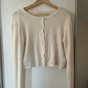 Ribbad beige kofta med knappar - Superfin ribbad kofta i beige med rund hals och knäppning framtill. Långärmad och croppad modell som är perfekt att slänga över en topp. Mjuk och skön, passar till allt och ger en clean look.