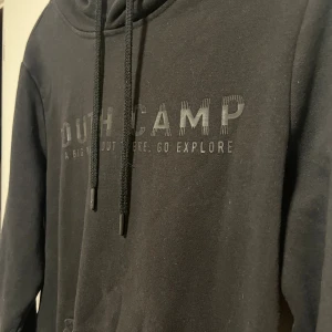 Svart hoodie från South Camp - Svart hoodie från South Camp med tryck på bröstet och texten 'IT'S A BIG WORLD OUT THERE. GO EXPLORE'. Tröjan har huva med snörning och en stor magficka. Perfekt för chill dagar och enkel att matcha med jeans eller joggers.