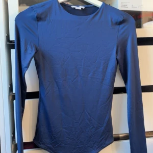Mörkblå långärmad body  - Säljer en mörkblå långärmad body från Amisu i storlek XS. Toppen har en tight passform och är tillverkad i ett mjukt, stretchigt material. Den har rund halsringning och en spetsig nederkant med knytband, vilket ger en unik look. Har aldrig använt, den har bara legat i garderoben💙💙