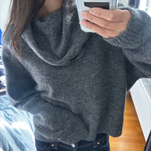 Mörkgrå stickad polotröja - Mysig mörkgrå stickad polotröja med oversized passform och bred polokrage. Tröjan har långa ärmar och ribbade muddar vid ärmslut och nederkant. Perfekt för kyliga dagar och enkel att styla med jeans eller kjol. 