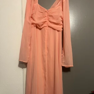 Ljusrosa långklänning med knappar - Superfin ljusrosa långklänning i flowigt tyg med långa ärmar och snygga knappar vid ärmsluten. 