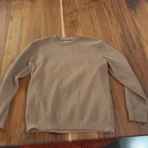 Beige stickad tröja från NN07 - Säljer en stilren beige stickad tröja från NN07. Tröjan har rund halsringning, ribbad struktur och långa ärmar. Perfekt för lager-på-lager och passar till både jeans och chinos. Enkel och clean design som funkar året runt.