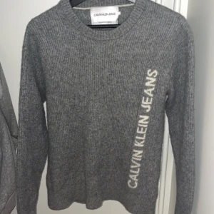 Grå stickad tröja Calvin Klein Jeans - Stickad grå tröja från Calvin Klein Jeans. Storlek M-S, ej använd                 