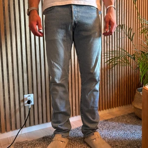 Levi's 501 ljusblå jeans straight fit - Klassiska Levi's 501 jeans i ljusblå denim med rak passform. Byxorna har normal midja, fem fickor och knappgylf. Perfekta för en avslappnad och tidlös look. Ikonisk röd Levi's-tag på bakfickan. 32/34