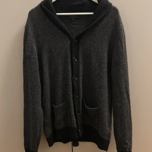 Mörkgrå kofta i lammull från M&S - Mysig mörkgrå kofta från M&S Collection i ren lammull. Koftan har knäppning framtill, två fickor och ribbade muddar. Perfekt för lager-på-lager och chill dagar. Regular fit och klassisk look.