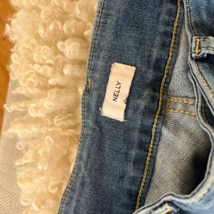 Blå jeans med fickdetaljer från Nelly - Snygga blå jeans från Nelly med raka ben och markerade sömmar längs framsidan. Byxorna har dubbla framfickor med lock och klassiska bakfickor. Jeansen är bootcut och har används en gång. Jeansen har normal passform och är tillverkade i klassiskt denimtyg. De är i väldigt bra skick! 