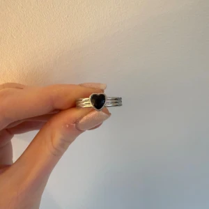 Silverring med svart hjärta - Snygg silverfärgad ring med ett svart hjärta i mitten. Ringen har tre band som går ihop och ger en cool detalj. Perfekt för dig som gillar unika smycken med lite edge och vill sticka ut.