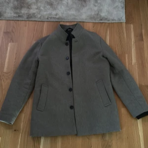 Grå ullrock med ståkrage - Rock i brun/grå färg storlek m köpt från Jack&Jones, kommer med en inbyggd väst, valfri kan tas bort eller läggas till genom dragkedja