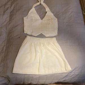 Sett omlottväst i linne-look & kjol - Säljer en sett  vit/beige väst med knyt i nacken och v-ringning. Västen har knappar framtill och två dekorativa fickor. Storlek 36.Materialet har en linnekänsla och västen har en croppad passform som ger en fräsch och modern vibe.tillhörande kjol med resor på baksidan. Mycket bra skick. Använd 1 gång. Passar storlek 34-36.säljer väldigt mycket kläder skicka gärna pm gör bra paketpris.