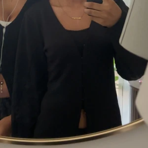 Svart kofta med knappar - En stilren svart kofta med knappar framtill. Koftan har lång ärm och en enkel, rak passform som funkar till många olika looks. Perfekt att slänga över ett linne eller t-shirt för en clean vibe.