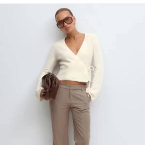 Vit omlottkofta från Gina Tricot - Superfin vit omlottkofta från Gina Tricot med knyt i sidan och v-ringad hals. Koftan är croppad, har långa ärmar och är stickad i mjukt material. Perfekt för lager-på-lager och snygg till både jeans och kostymbyxor. Aldrig använd, säljer då den är lite för stor❣️