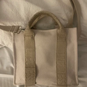 Beige axelväska från Zara i canvas - Säljer en stilren beige axelväska från Zara i kraftig canvas. Väskan har både handtag och justerbar axelrem, samt diskret logga på sidan. Perfekt storlek för det viktigaste och enkel att matcha till olika outfits.