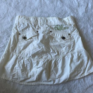 Vit cargokjol från Peak Performance - Supersöt vit cargo kjol från Peak Performance med volangkant och coola fickor med knappar bak. Storlek S. Några små fläckar på framsidan men går säkert bort i tvätten💕
