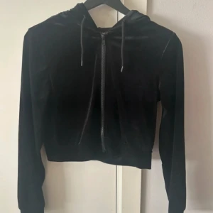 Svart sammetshoodie från Monki XXS - Svart croppad hoodie från Monki i mjuk sammet med dragkedja framtill och snörning i huvan. Långärmad och perfekt för en chill och trendig look. Passar dig som gillar en lite mer fitted stil.