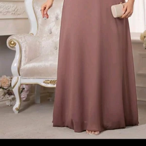 Lång  klänning med puffärm - Elegant långklänning i en mjuk  nyans med vackra puffärmar. Klänningen har en klassisk, svepande siluett och är tillverkad i ett lätt, flytande material som ger ett exklusivt intryck. Perfekt för dig som vill sticka ut med en stilren och tidlös look.