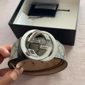 Gucci bälte med silver-spänne - Säljer mitt fina Gucci bälte då det har växt ur mig. Bältet har klassiskt monogrammönster i beige och grå toner, tillverkat i skinn och canvas. Kommer med original ask. dustbag och kvitto. Perfekt för en stilren outfit! 