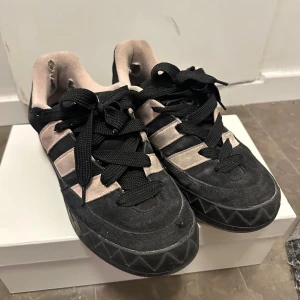 Adidas adimatic  - Adidas sneakers i svart mocka med klassiska beige ränder och logga på hälen. Skorna har rund tå, platt sula med mönster och svart snörning. Insidan är beige och materialet är mocka och syntet. Perfekt för dig som gillar sportig stil och streetwear.