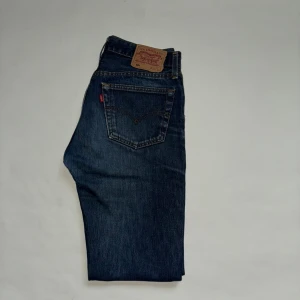 Levi's 501 mörkblå jeans W32 L32 - Klassiska Levi's 501 jeans i mörkblå tvätt med raka ben. Snygga kontrastsömmar och ikonisk läderpatch baktill. Jeansen har fem fickor och är tillverkade i slitstarkt bomullsdenim. Perfekta för dig som gillar tidlös stil och vill ha ett par jeans som alltid funkar.