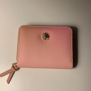 Plånbok rosa/orange - En plånbok som är ombre färgad i rosa/orange med guldiga detaljer. Har en guldig sol på framsidan. Svart insida olika fack. Är köpt från spanien. En oanvänd praktisk plånbok att kunna ha i väskan!