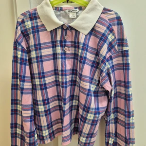 Rutig pikémagtröja från Monki XS - Superfin pikétröja från Monki i storlek XS med rutigt mönster i rosa, blått, vitt och lite gult. Tröjan har klassisk vit krage, knappar framtill och är långärmad. Tillverkad i 100% bomull för en skön och avslappnad känsla.