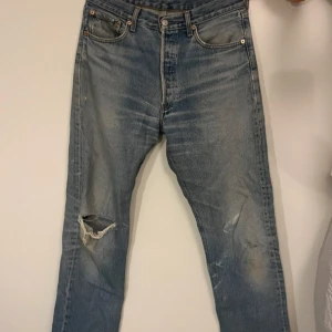  Levis 501 - Levi's 501 jeans i ljusblå tvätt med klassisk rak passform. Jeansen har slitningar och hål på ena knät för en snygg look. Riktigt snygga vintage jeans. 33/34, skulle säga att de passar W32 bättre. Pris kan absolut diskuteras.