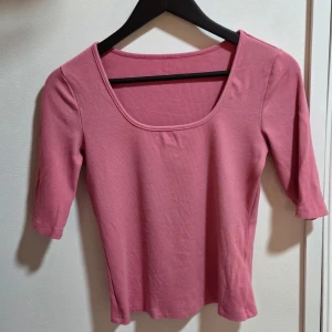 Rosa ribbad topp med fyrkantig hals, M - Säljer en ljusrosa ribbad topp med snygg fyrkantig halsringning och trekvartsärm. Materialet är mjukt och stretchigt, troligen bomull eller syntet. Enkel och clean design som är lätt att matcha med jeans eller kjol. Perfekt för dig som gillar basic men ändå vill ha lite färg.