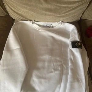 Vit sweatshirt från Stone Island - Vit sweatshirt från Stone Island med klassisk rund hals och ikonisk logotyp-patch på vänster ärm. Tröjan är i mjuk bomull och har en clean, stilren look som passar perfekt till jeans eller trackpants. Köpt på NK i Stockholm för 3-4 år sedan. Har använts totalt 2 gånger sen har den bara legat i garderoben… några mer frågor, bara hör av dig.