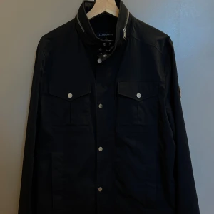 Svart fältjacka från J.Lindeberg - Svart fältjacak från J.Lindeberg i storlek 48. Passar en perfekt som har S/M. Den är i väldigt bra skick inga skador eller liknande. Stilren design med lång ärm och normal passform. 