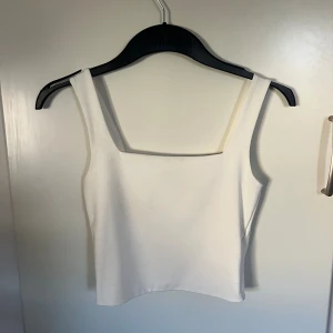 Vit linnetopp från Amisu - Säljer en stilren vit linnetopp från Amisu med breda axelband och fyrkantig ringning. Toppen är enkel och passar perfekt till jeans eller kjol. Materialet känns mjukt och stretchigt, vilket gör den bekväm att bära hela dagen.