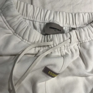Vita Essentials mjukisbyxor med snörning - Priset kan diskuteras!!Säljer ett par vita mjukisbyxor från Essentials Fear of God. Byxorna har elastisk midja med snörning, muddar vid benslut och tryckt logga på benet. Sköna och stilrena, perfekta för chill dagar. Materialet är mjukt och känns riktigt bekvämt.