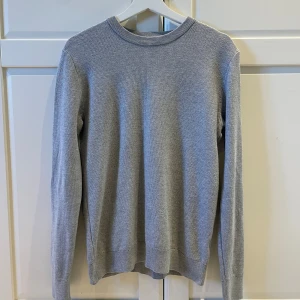 Grå stickad tröja från Cubus - Säljer en stilren grå stickad tröja från Cubus i storlek S. Tröjan har rund hals, ribbade muddar och ett diskret, strukturerat stickat mönster. Perfekt för dig som gillar enkel och clean look med långärmad passform.