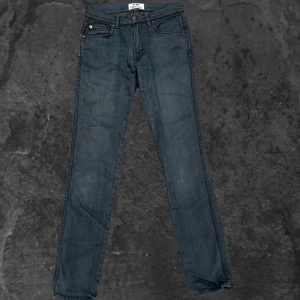 Acne Studios jeans  - Mörkblå raka jeans från Acne Studios, modell Ace Coral. Klassisk femficksdesign med orangea sömmar och metallknappar. Tillverkade i bomull med lite elastan för extra komfort. Perfekta för dig som gillar stilrena och tidlösa jeans.