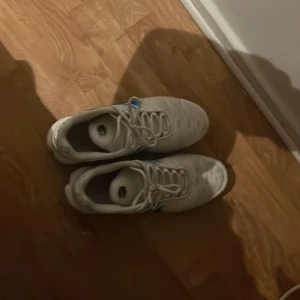 Nike Air Max Plus vita/blå sneakers storlek 42,5 - Nike Air Max Plus sneakers i vitt och blått med gula detaljer. Skorna har en sportig vibe, synlig Air Max-dämpning och snörning. Ovandelen är i syntetmaterial med vågiga linjer och den klassiska swoosh-loggan på sidan. Perfekta för dig som gillar streetwear och vill sticka ut.